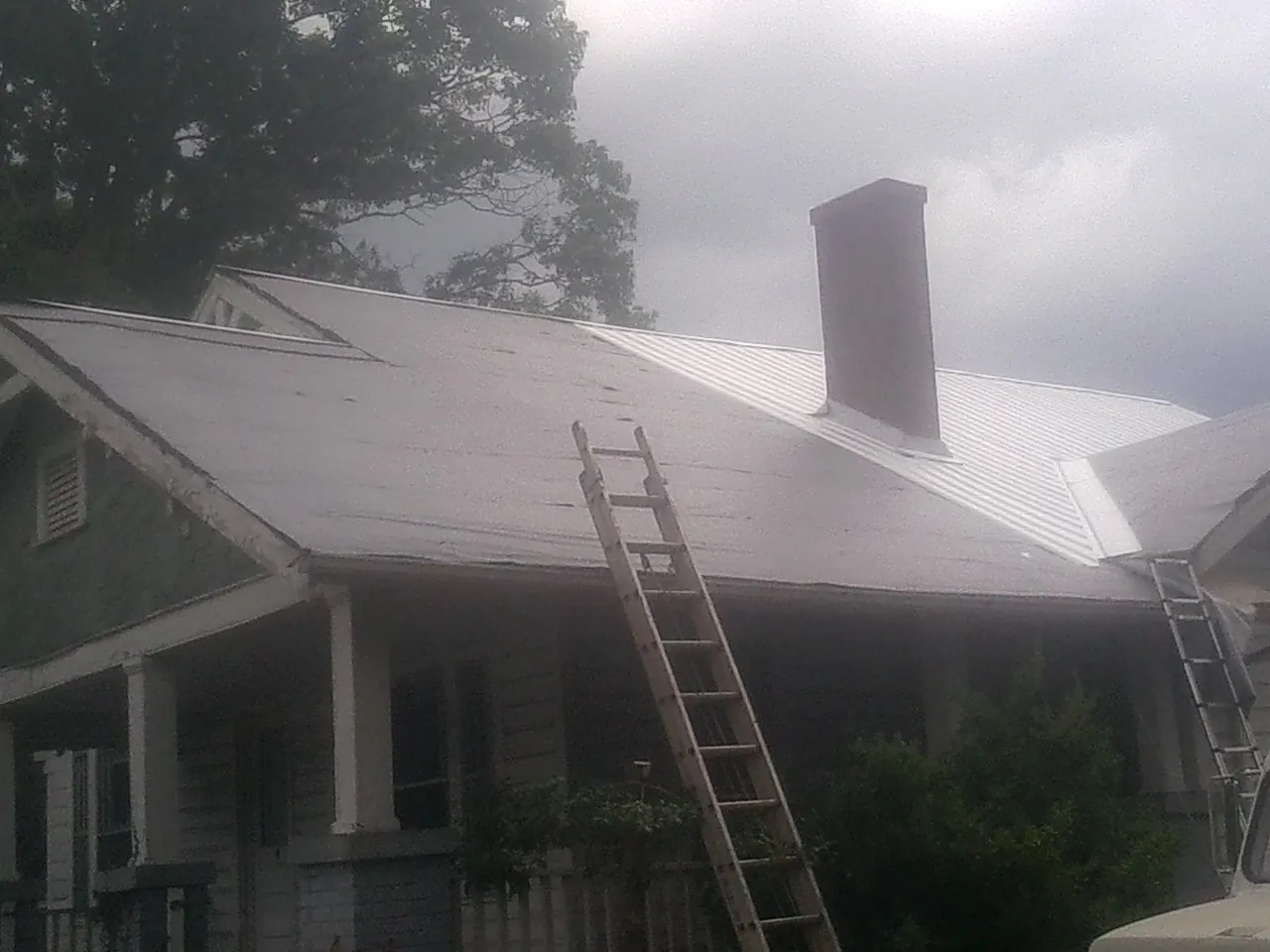 Ladders against a metal roof on an older home with a brick chimney in Sparta